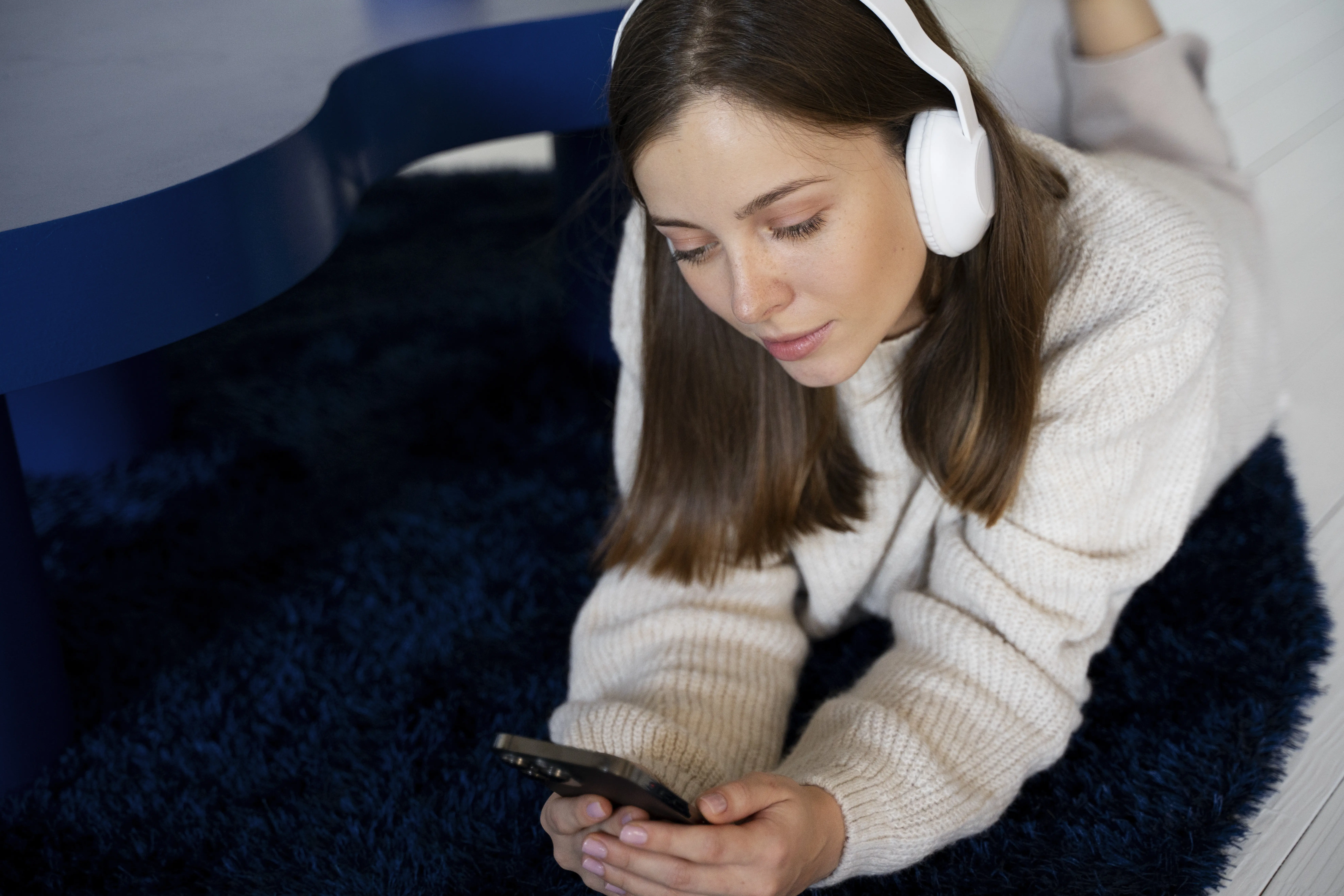 Eine junge Frau hört Musik mit ihrem Smartphone, während sie auf dem Boden liegt.