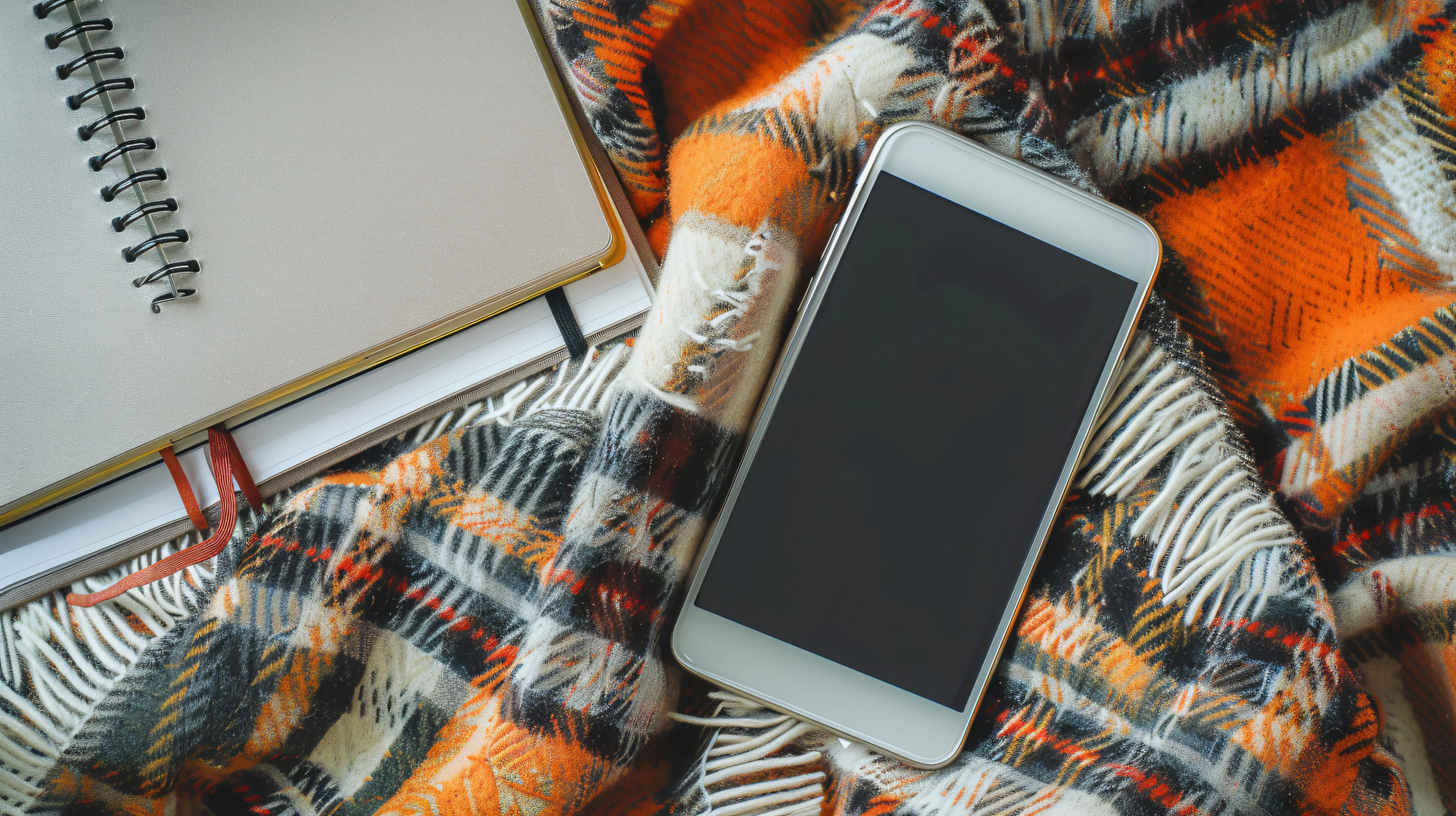 Moderne Flatlay-Komposition mit einem Handy auf einer karierten Decke und einem Notizbuch.