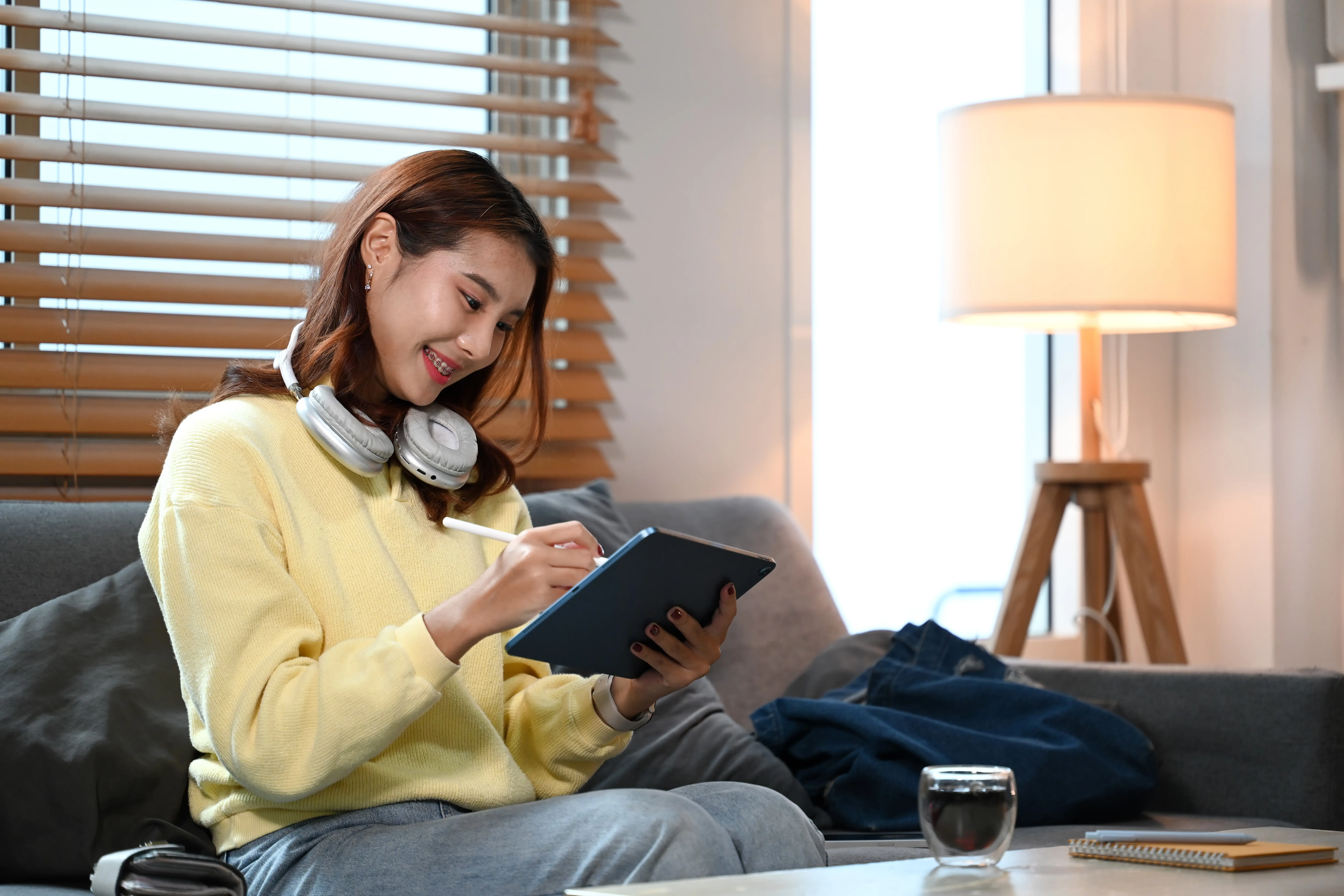 Eine lächelnde junge Frau mit Kopfhörer arbeitet zu Hause an einem Designprojekt auf einem digitalen Tablet.